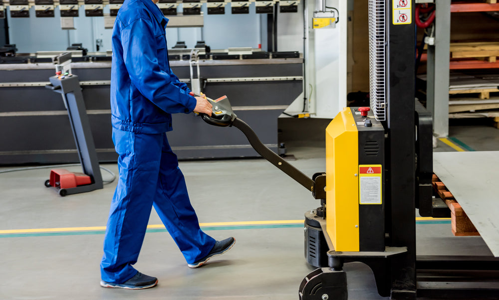 A worker in a warehouse uses a hand pallet stacker to transport pallets.