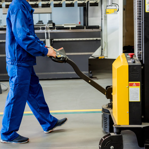 A worker in a warehouse uses a hand pallet stacker to transport pallets.